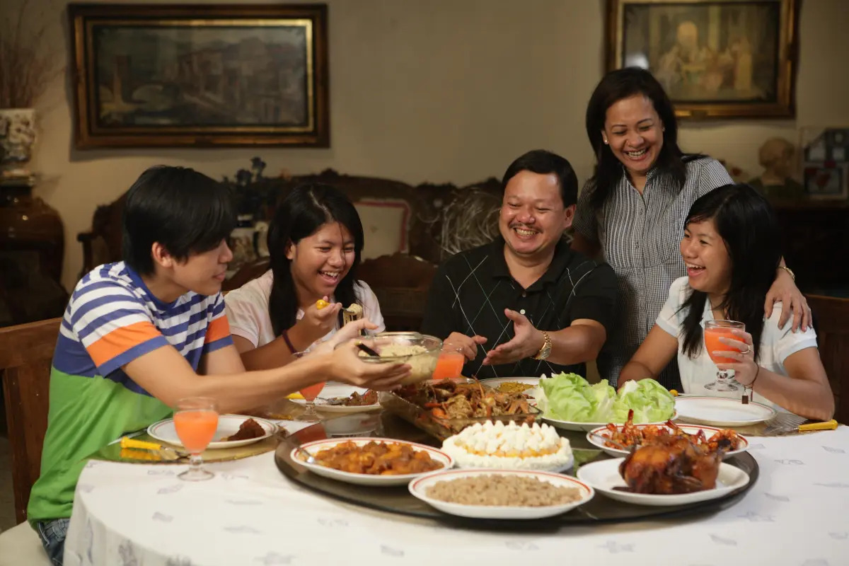 Family of four people eating and laughing together at home.